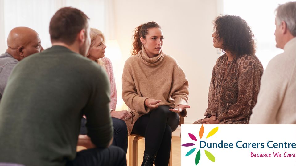 Mixed group of people sitting on chairs having a discussion. Dundee Carers Centre logo bottom right.