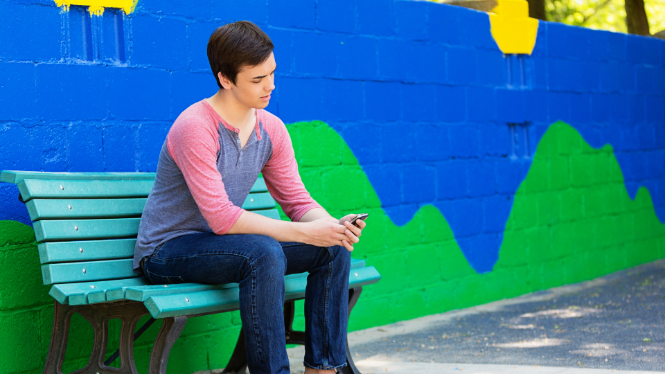 Young man sitting on a colourful blue bench against a painted brick wall