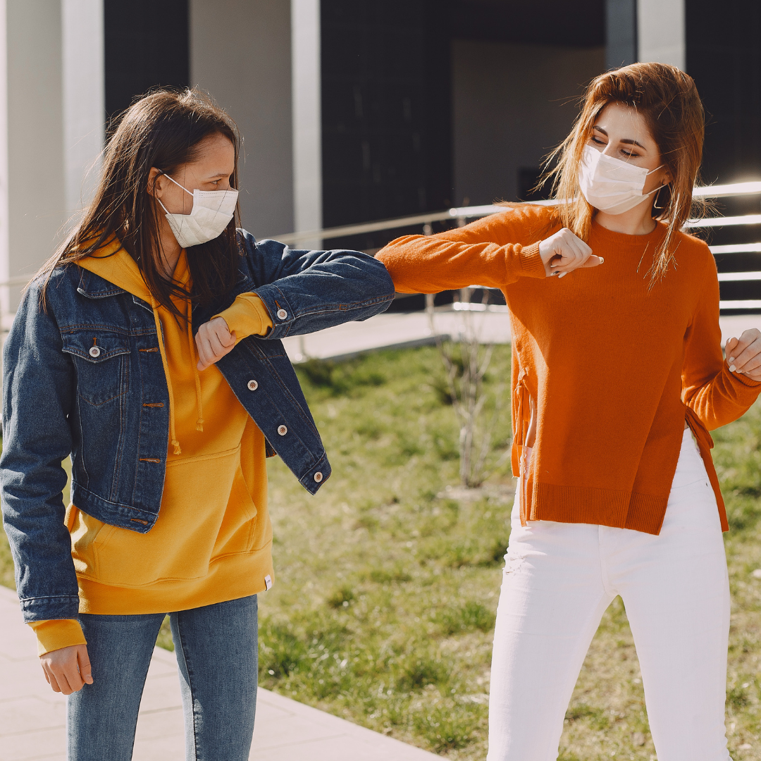 Two girls wearing facemasks walking together. Girls are bumping elbows as a safe form of shaking hands.