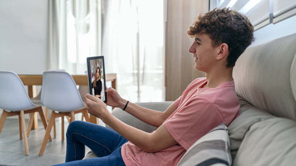 Teenage boy sitting on a sofa chatting to someone via video call on a mobile device